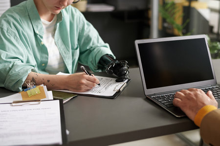 Young woman with disability filing document while having meeting with consultant in officeの写真素材