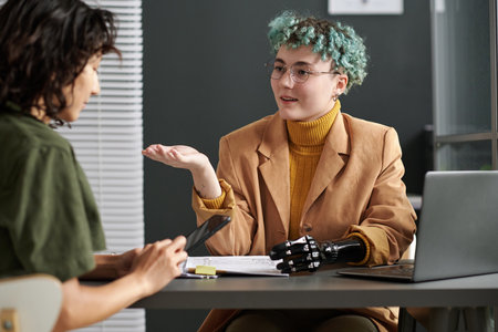 Young businesswoman with prosthetic arm talking to customer during their meeting in officeの写真素材