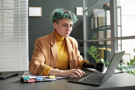 Serious businesswoman with disability concentrating on her online work on laptop in officeの写真素材