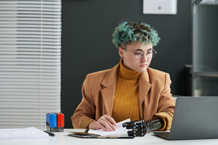 Young social worker with prosthetic arm working in office with documentsの写真素材