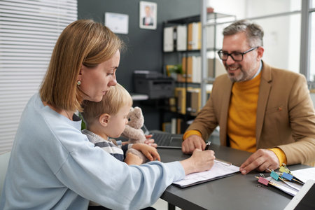 Young woman sitting with her little son and filing documents for social benefitsの写真素材