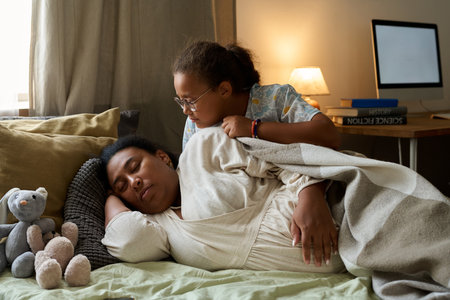 Daughter sitting on bed near her pregnant mother while she sleepingの写真素材