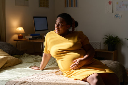 African American pregnant woman stroking her pregnant belly and resting on bedの写真素材