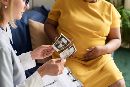Close-up of nurse examining ultrasound image of baby and talking to pregnant womanの写真素材
