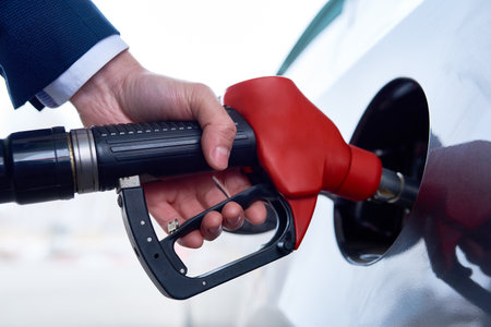 Closeup of unrecognizable businessman refueling gas tank of black luxury car with hand holding pump nozzleの写真素材