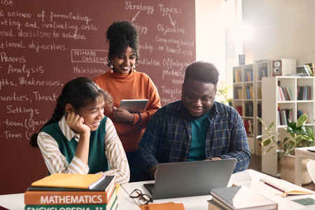 Portrait of three Black college students looking at laptop screen in class and smiling cheerfullyの写真素材