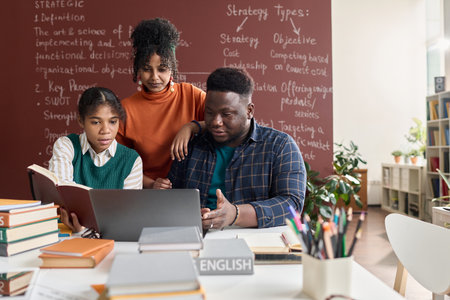 Front view portrait of three Black young people using laptop together while working on group project in schoolの写真素材
