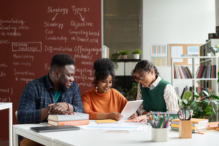 Group of three African American teenagers enjoying work together in college classroom and using digital tabletの写真素材