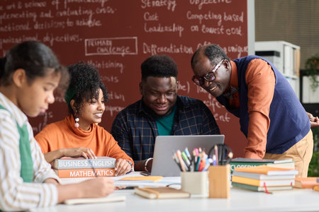Smiling Black teacher helping students working on group project together and using laptopの写真素材