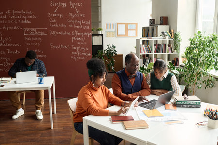 Wide angle view at African American girls working with senior professor and using computer devices in college classroom copy spaceの写真素材