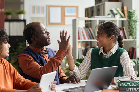 Portrait of smiling African American girl high five with senior professor while working on project in school classroomの写真素材