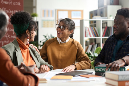 Group of young African American students enjoying discussion sitting at table together in class, focus on girl smiling happilyの写真素材