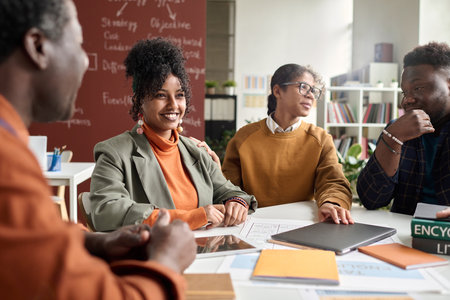 Portrait of smiling curly haired girl enjoying discussion on group project with students in college copy spaceの写真素材