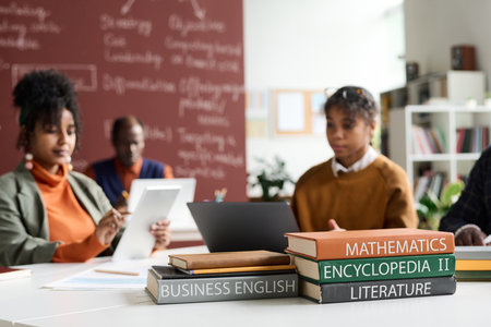 Close up of textbooks on school subjects math, business and literature on desk in college classroom with students in background copy spaceの写真素材