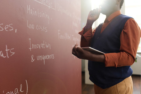 Closeup of senior African American college professor writing on chalkboard while preparing for lecture in collegeの写真素材