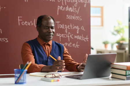 Portrait of senior Black college professor sitting at desk and using computer, copy spaceの写真素材