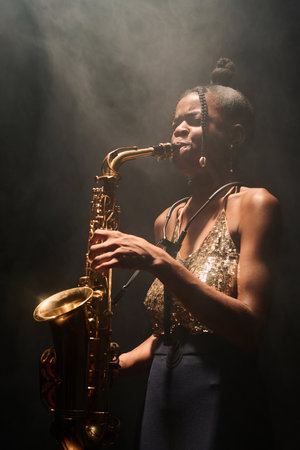 Side view portrait of young Black woman playing saxophone jazz music in spotlightの写真素材