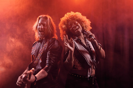 Waist up portrait of soul band performing on stage in nightclub African American woman singing with guitaristの写真素材