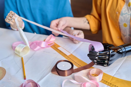 Close up of two girls with disability working in inclusive atelier studio and holding ribbons with prosthetic hands copy spaceの写真素材