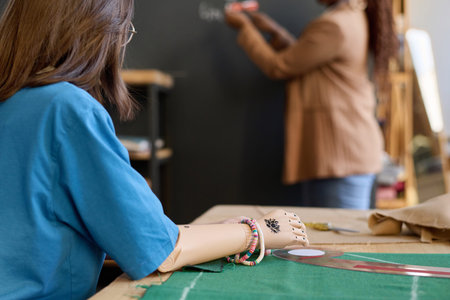 Close up of teenage girl with prosthetic hand listening to teacher in sewing class copy space