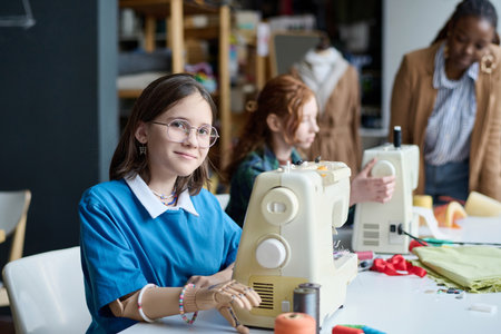 Side view portrait of young girl with prosthetic hand using sewing machine in classroom and looking at cameraの写真素材