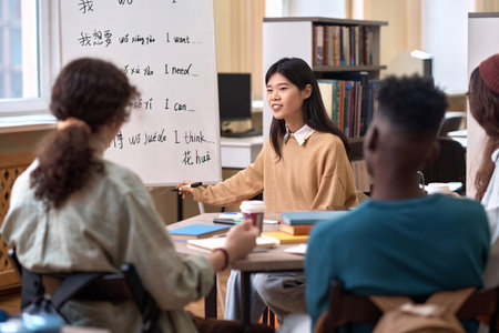 Portrait of smiling Asian female teacher explaining Chinese language grammar to students in library copy spaceの写真素材