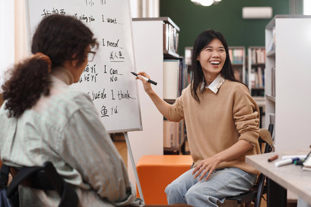 Portrait of young Asian woman laughing cheerfully pointing at whiteboard with hieroglyphs and enjoying fun Chinese language lesson copy spaceの写真素材