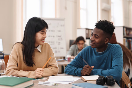 Side view portrait of smiling Asian woman looking at Black student while studying together in college libraryの写真素材