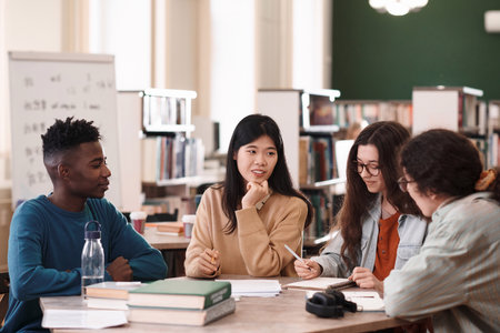 International group of students sitting at table in college library and studying together with focus on young Asian womanの写真素材
