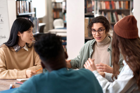 Portrait of long haired male student presenting ideas to students during group discussion in libraryの写真素材