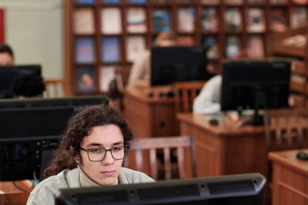 Cropped shot of young Middle Eastern male student wearing glasses and looking at computer screen in...
