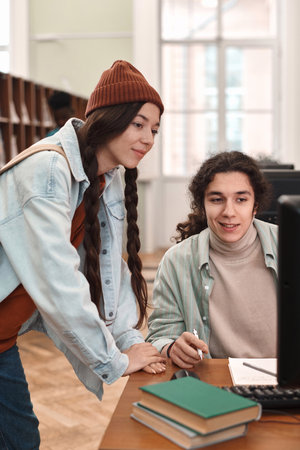 Vertical portrait of two young students in college library looking at computer screen togetherの写真素材