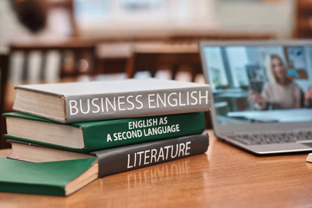 Close up background image of stack of books on English language in school library with video lecture on laptop screen in background, copy spaceの写真素材
