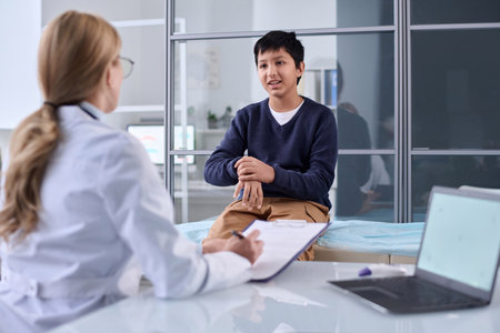 Portrait of young boy explaining symptoms of hand and wrist pain to pediatrician in clinicの写真素材