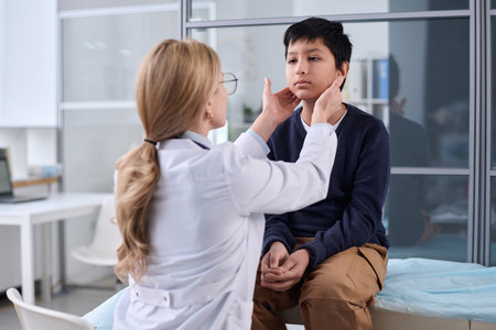 Back view of female doctor examining neck and throat of young boy during health check up in pediatric clinicの写真素材