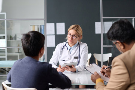 Portrait of expert woman doctor consulting Middle Eastern family while sitting at table in clinic officeの写真素材