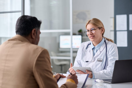 Portrait of smiling female doctor talking to Middle eastern man during consultation in medical clinicの写真素材