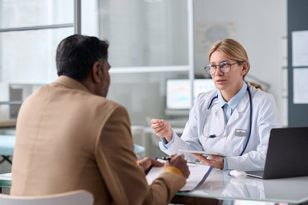 Portrait of smiling female doctor consulting Middle Eastern man sitting across table in medical clinicの写真素材