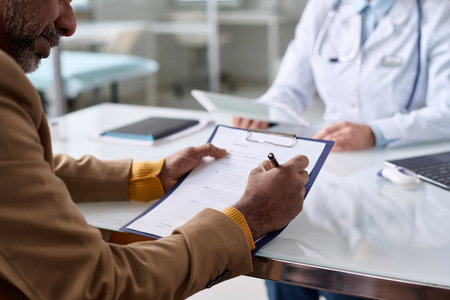 Over shoulder view of mature Middle Eastern man writing on clipboard in clinic and filling in medical information copy spaceの写真素材