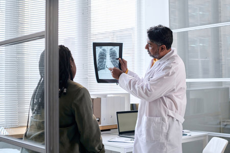 Side view portrait of senior doctor pointing at chest x ray while consulting patient in clinic copy spaceの写真素材