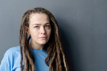 Minimal portrait of young Caucasian woman with long dreadlocks looking at camera standing on grey background copy spaceの写真素材