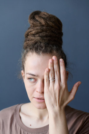 Vertical close up of Caucasian woman with dreadlocks in bun hairstyle covering face with handの写真素材