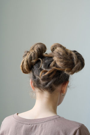 Vertical back view of young woman with dreadlocks space buns hairstyle on whiteの写真素材