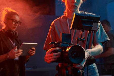 Cropped shot of female cameraman operating equipment in studio set with neon lights copy space