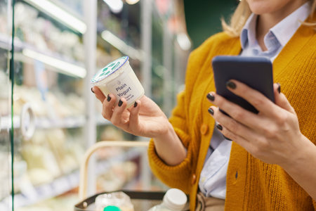 Close up of unrecognizable woman buying dairy products in supermarket and using smartphone, copy spaceの写真素材