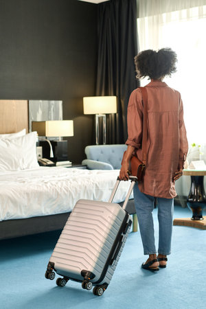 Full length back view of young Black woman suitcase arriving at resort and entering hotel room with suitcaseの写真素材
