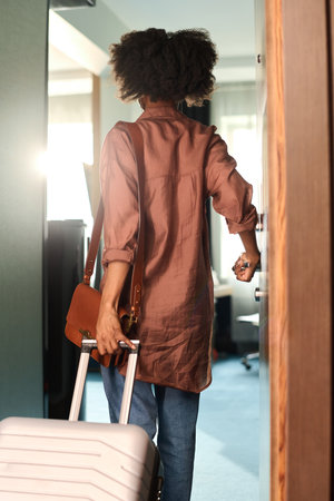 Vertical back view of young African American woman opening door to hotel room and holding suitcaseの写真素材