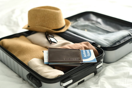 Background image of open suitcase with passport and airplane ticket on bed in hotel room travel conceptの写真素材