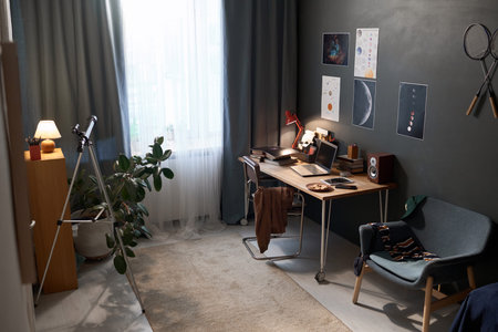Wide angle shot of teenage boys room interior with workplace desk and hobby equipment for astronomy...