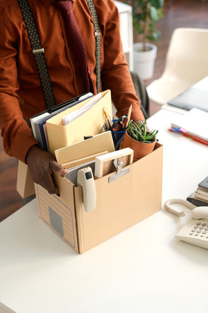 Vertical closeup of person holding box with personal items at workplace table and unpacking for new jobの写真素材